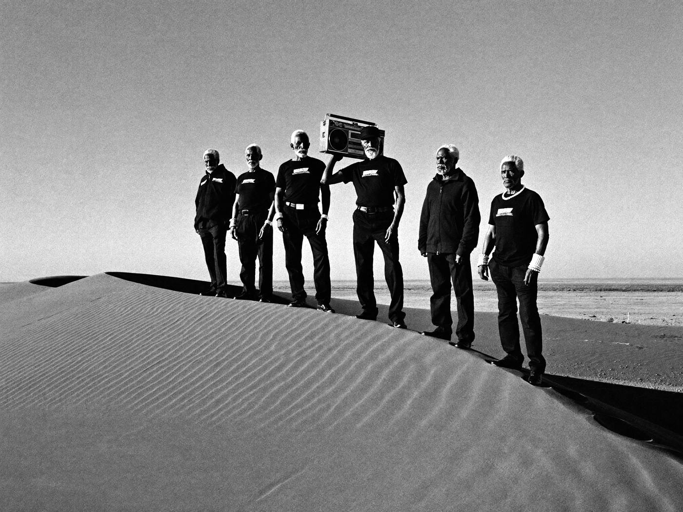 Six elders in black standing on a desert dune